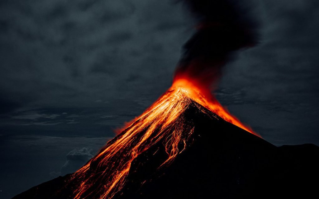 A volcano glowing with lava against a dark night sky