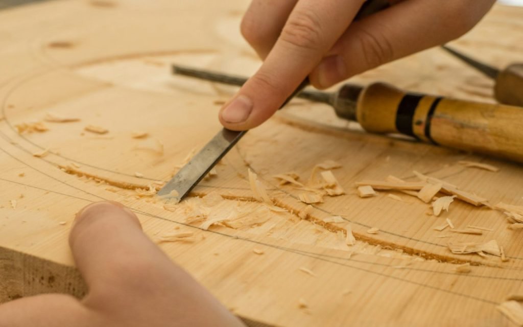 Hands sanding a plain wooden board in a small workshop